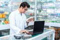 Portrait of young male pharmacist holding medication while using laptop at pharmacy counter Royalty Free Stock Photo