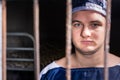 Portrait of young male prisoner standing behind a prison grid in Royalty Free Stock Photo