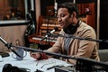 Portrait of young male radio host having a drink, looking focused while speaking in microphone, moderating a live show Royalty Free Stock Photo