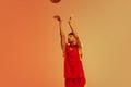 Portrait of young man, basketball player throwing ball into basket isolated over orange studio background in neon light Royalty Free Stock Photo