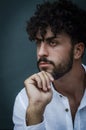 Portrait of a young man with beard and curly hair, holding his chin with his hand and looking thoughtful Royalty Free Stock Photo