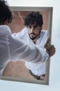 Portrait of a young man with beard and curly hair, who looks at himself while holding a mirror in his hands Royalty Free Stock Photo