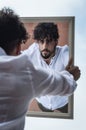 Portrait of a young man with beard and curly hair, who looks at himself while holding a mirror in his hands Royalty Free Stock Photo