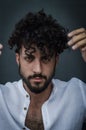 Portrait of a young man with a beard, with his hands raised to move his hair away from his face