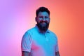 Portrait of young man with beard smiling looking at camera in neon light against vibrant gradient studio background. Royalty Free Stock Photo