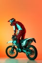 Portrait of young man, biker in full equipments riding motorbike isolated over orange studio background in neon light