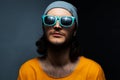Portrait of young man on black and grey background, wearing blue sunglasses, hat and orange shirt. Royalty Free Stock Photo