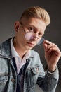 Portrait of young man with blonde hair posing in sunglasses and jeans jacket isolated over grey background. Casual style Royalty Free Stock Photo