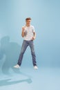 Portrait of young man in casual clothes cheerfully jumping, posing isolated over blue studio background. Success and Royalty Free Stock Photo