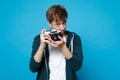 Portrait of young man in casual clothes holding taking pictures on retro vintage photo camera isolated on blue wall Royalty Free Stock Photo