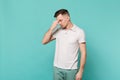 Portrait of young man in casual clothes with lowered head putting hand on nose isolated on blue turquoise wall Royalty Free Stock Photo