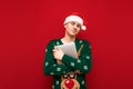 Portrait of young man in christmas clothes posing on red background with laptop in hand. Photo of freelancer at christmas, holding