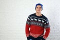 Portrait of young man in Christmas sweater and hat near white brick wall Royalty Free Stock Photo