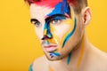 Portrait of young man with colored face paint on yellow background. Professional Makeup Fashion. fantasy art makeup