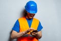 Portrait of young man construction worker engineer, typing on smartphone, wearing safety equipment on grey textured background. Royalty Free Stock Photo