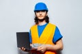 Portrait of young man construction worker engineer wearing safety equipment, holding laptop on background of grey textured wall. Royalty Free Stock Photo