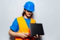 Portrait of young man construction worker engineer wearing safety equipment, holding laptop on textured background of grey. Royalty Free Stock Photo