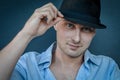 Portrait of a young man fixing a black hat on his head with two fingers