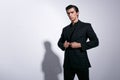 Elegant young man in full black costume, arranged his jacket, looking serious at camera, isolated on a white background. Royalty Free Stock Photo