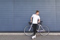 Portrait of a young man in full height standing beside a white bicycle against the wall and looking sideways Royalty Free Stock Photo