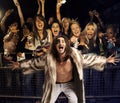 Portrait of young man in fur coat screaming with excited audience in the background Royalty Free Stock Photo
