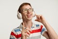 Portrait of young man in glasses posing, listening to online lesson in headphones isolated over white studio background Royalty Free Stock Photo