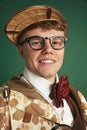 Portrait of young man in glasses, wearing vintage costume of detective, smiling, looking at camera against green studio Royalty Free Stock Photo