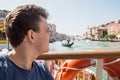 Portrait of a young man on a Grand Canal cruise on the bow of a river tram. The look is directed to the horizon.