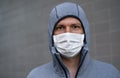 Portrait of young man in gray hoodie and home made cotton face mouth virus mask, gray wall in background
