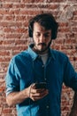 Portrait of young man with headphones and cell phone. Casual wear and brick wall of background Royalty Free Stock Photo