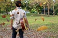 Portrait of young man holding acoustic guitar against among falling leaves in the park