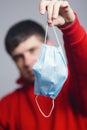 Portrait of young man holding medical protective mask on studio background, boy take off flu mask, concept of personal Royalty Free Stock Photo