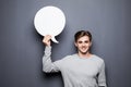 Portrait of Young man holding white blank speech bubble with space for text isolated on grey background. Royalty Free Stock Photo