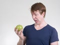 Portrait of young man looking disgusted while holding apple