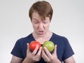 Portrait of young man looking disgusted while holding tomato and apple