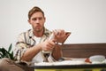 Portrait of young man looking serious at his suitcase with clothes, going through the check-list, holding notebook with Royalty Free Stock Photo