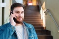 Portrait young man making call on hallway stairs. Caucasian bearded business man in modern city office have mobile conversation, Royalty Free Stock Photo