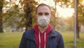Portrait of a young man in a medical disposable protective mask. A man stands in an autumn public place in a park and