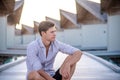Portrait of young man model posing in expensive clothes sitting near water bungalows at the tropical island luxury resort