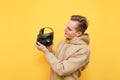 Portrait of a young man in a pink sweater stands with a VR helmet for playing on a yellow background and looking a gadget with