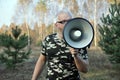 Portrait of a young man screaming with a megaphone in the forest. Lost People Search Concept