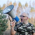 Portrait of a young man screaming with a megaphone in the forest. Lost People Search Concept