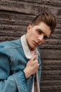 Portrait young man with serious face with trendy hairstyle in fashionable blue denim casual jacket near vintage wooden wall on Royalty Free Stock Photo