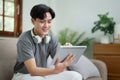 A portrait of a young man showing a smiling face while relaxing, using a tablet computer and a pair of headphones to Royalty Free Stock Photo