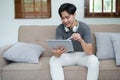 A portrait of a young man showing a smiling face while relaxing, using a tablet computer and a pair of headphones to Royalty Free Stock Photo