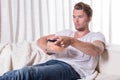 Portrait young man sitting on couch and eating chips and zapping