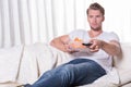 Portrait young man sitting on couch and eating chips and zapping Royalty Free Stock Photo