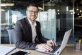 Portrait of a young man sitting at a desk in an office center in a suit and working on a laptop. Looking and smiling at Royalty Free Stock Photo