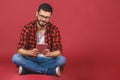 Portrait of young man sitting on the floor using a tablet pc, isolated against red background. Ready for your design Royalty Free Stock Photo
