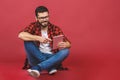 Portrait of young man sitting on the floor using a tablet pc, isolated against red background. Ready for your design Royalty Free Stock Photo